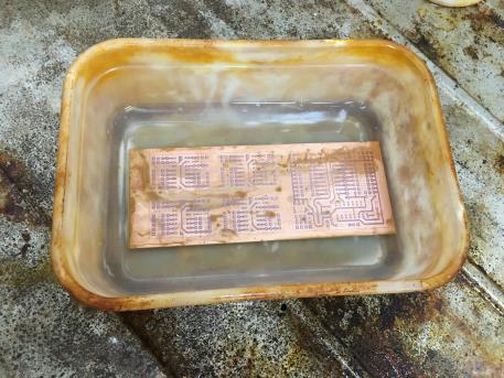 The copper-clad board partway through etching, the printed circuit pattern still visible under the developer solution